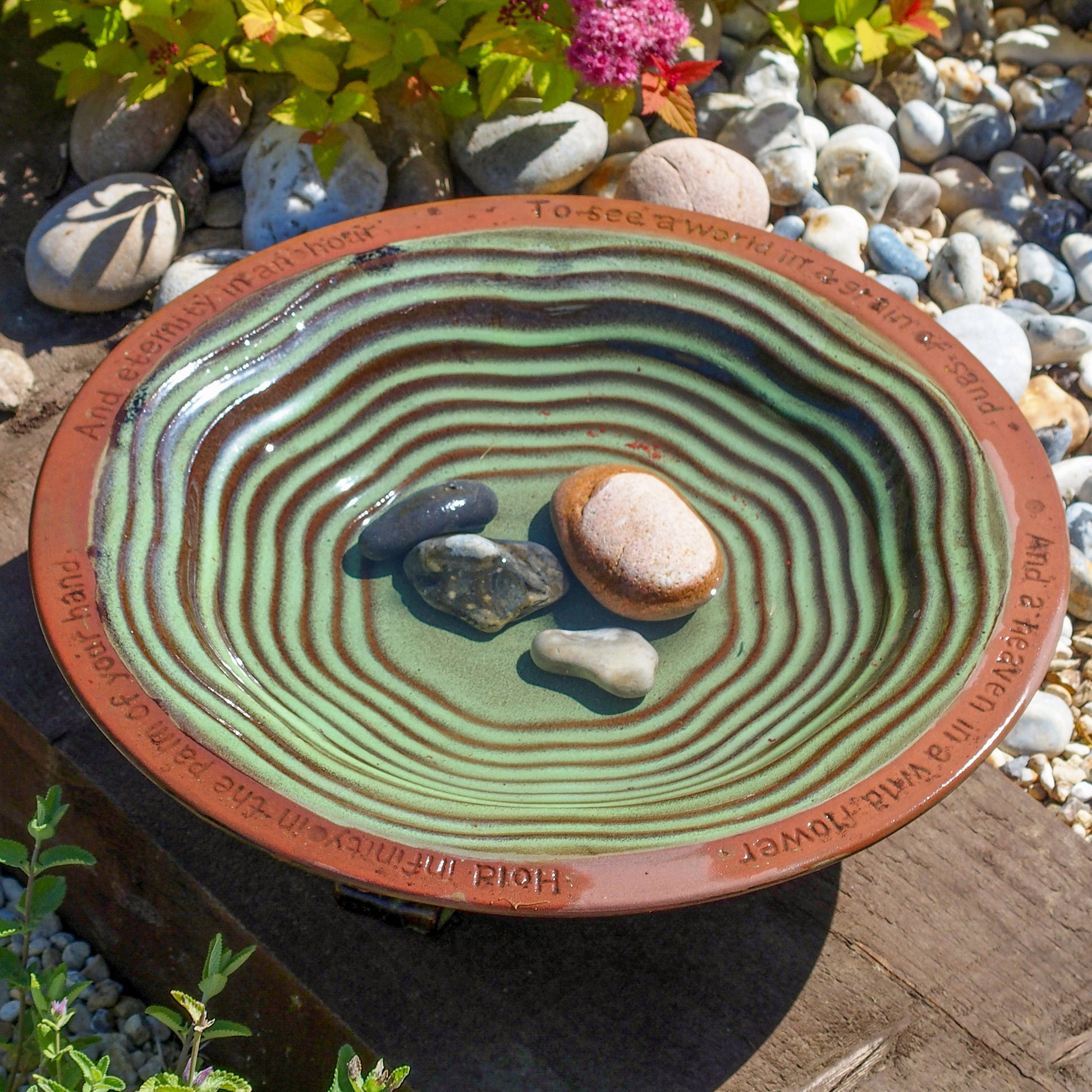 The Echoes Bird Bath on a raised wooden surface with pebbles placed inside it.