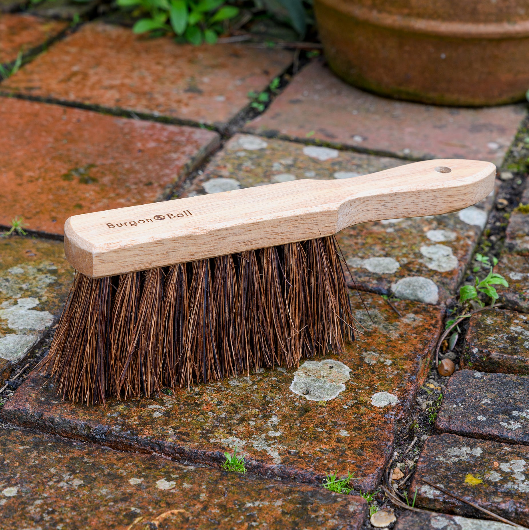 Wooden hand sweeping brush with natural bristles on paving.