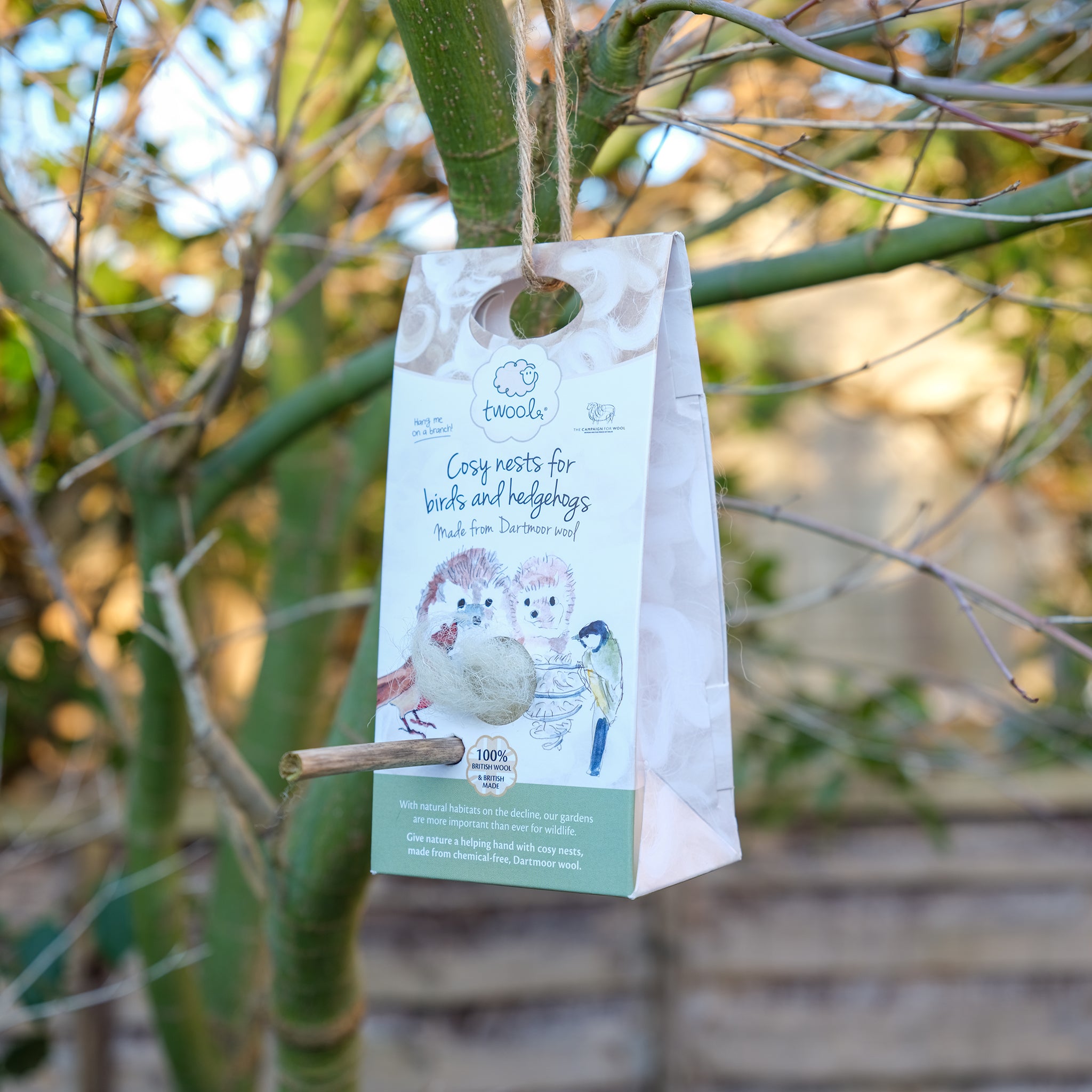 Packet of nesting wool hanging from a tree branch with a stick pushed through to help birds collect wool.