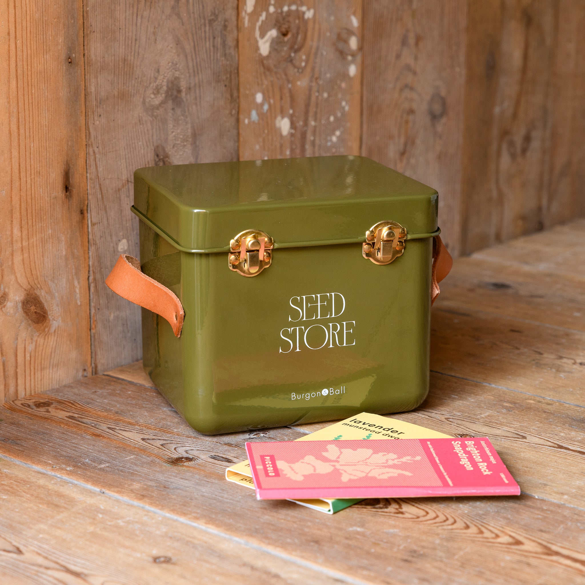 Seed packet storage tin in olive placed on a wooden surface with a wooden background.