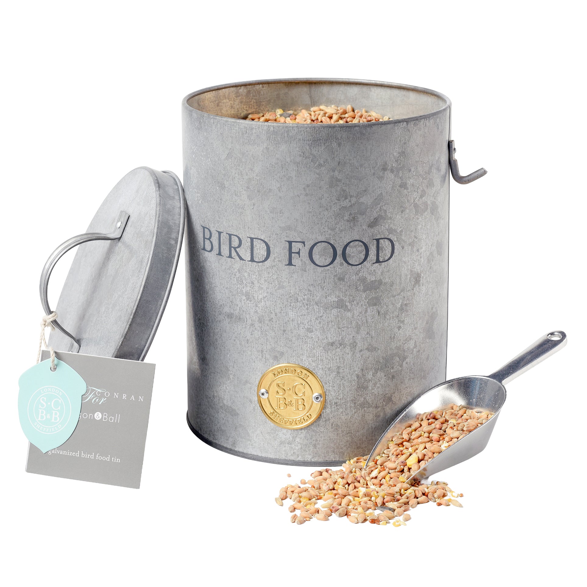 Galvanised steel bird food tin full of seeds, with its lid off and scoop next to it.