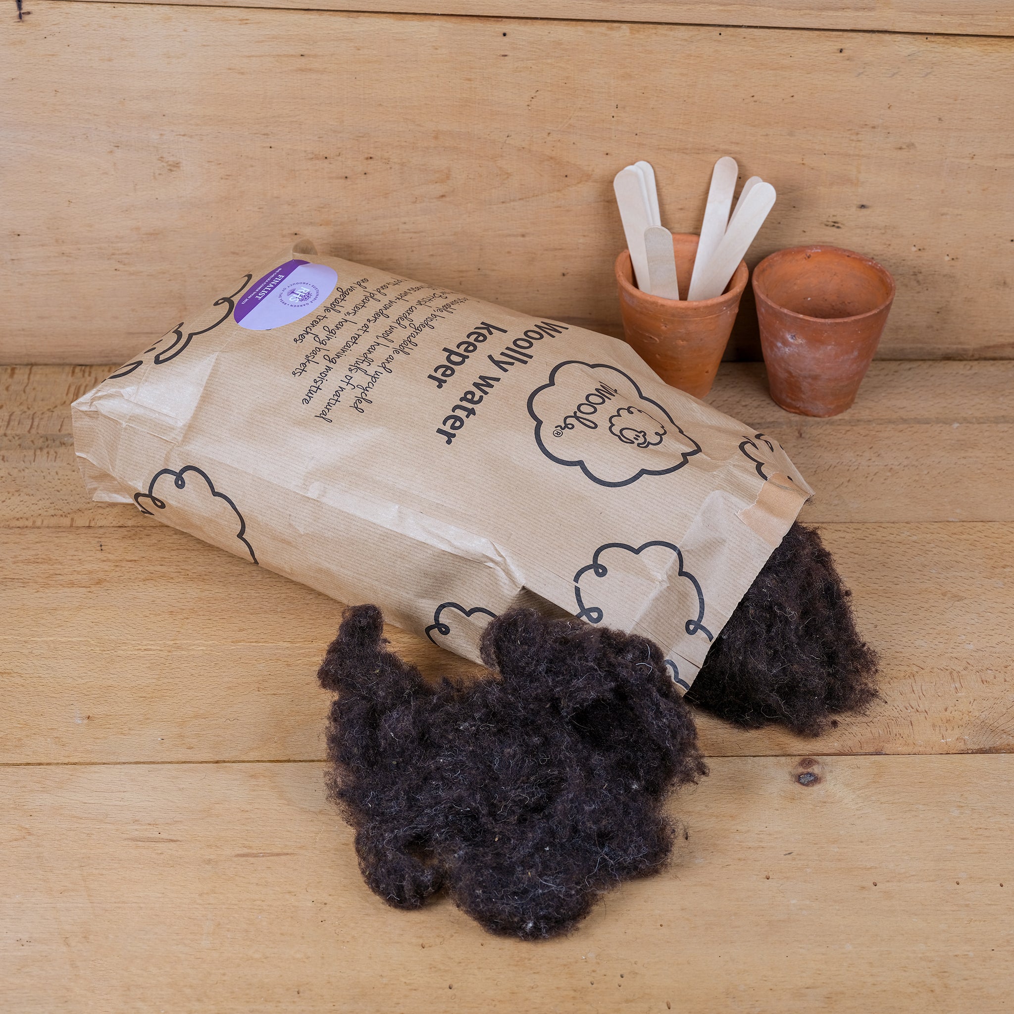 A large brown paper bag of Twool’s Woolly Water Keeper consisting of fluffy, undyed natural wool, used for mixing with compost to improve moisture retention.